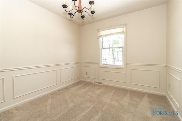 unfurnished room with light colored carpet, a wainscoted wall, visible vents, and an inviting chandelier