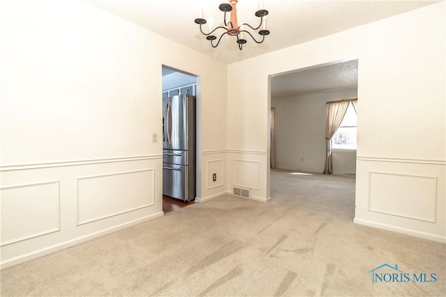 empty room with carpet floors, visible vents, a decorative wall, a textured ceiling, and a chandelier