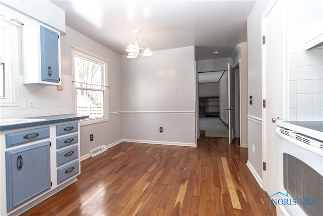 unfurnished dining area featuring baseboards, dark wood-style flooring, visible vents, and a notable chandelier