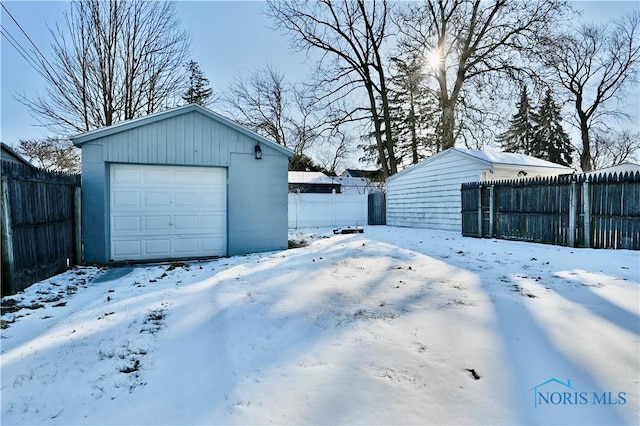 snow covered garage with a detached garage and fence