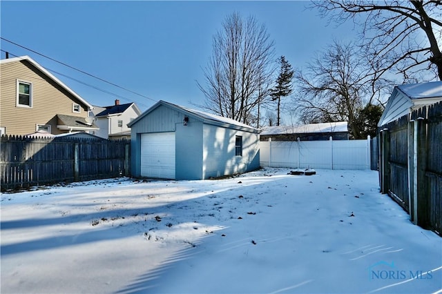 snowy yard featuring a fenced backyard, a detached garage, and an outdoor structure