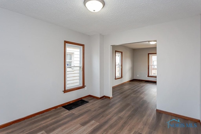 spare room with a textured ceiling, dark wood-type flooring, visible vents, and baseboards