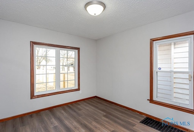 spare room featuring baseboards, visible vents, dark wood finished floors, and a textured ceiling