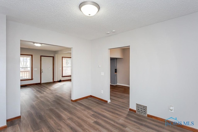 spare room with a textured ceiling, wood finished floors, visible vents, and baseboards