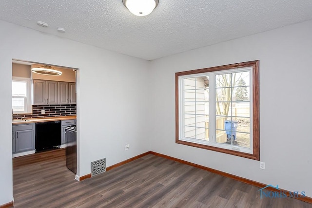 interior space with a textured ceiling, a sink, visible vents, baseboards, and dark wood-style floors