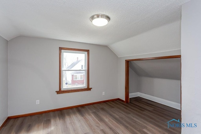 additional living space featuring a textured ceiling, wood finished floors, lofted ceiling, and baseboards