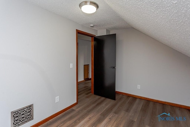 additional living space with baseboards, a textured ceiling, visible vents, and wood finished floors