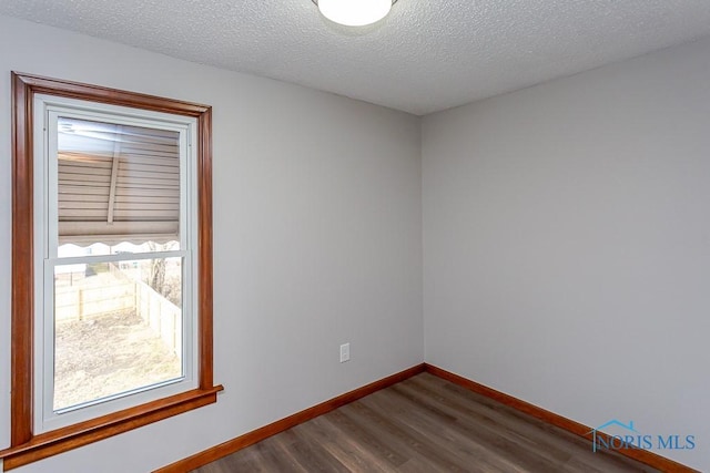 unfurnished room with dark wood-type flooring, a textured ceiling, and baseboards