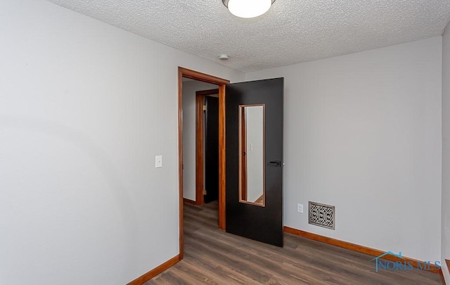 spare room with a textured ceiling, wood finished floors, visible vents, and baseboards