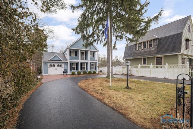 view of front facade with aphalt driveway, fence private yard, a gambrel roof, roof with shingles, and a front lawn