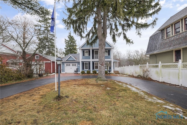 traditional-style home featuring aphalt driveway, a front yard, and fence