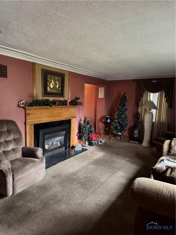 carpeted living room featuring a glass covered fireplace, visible vents, crown molding, and a textured ceiling