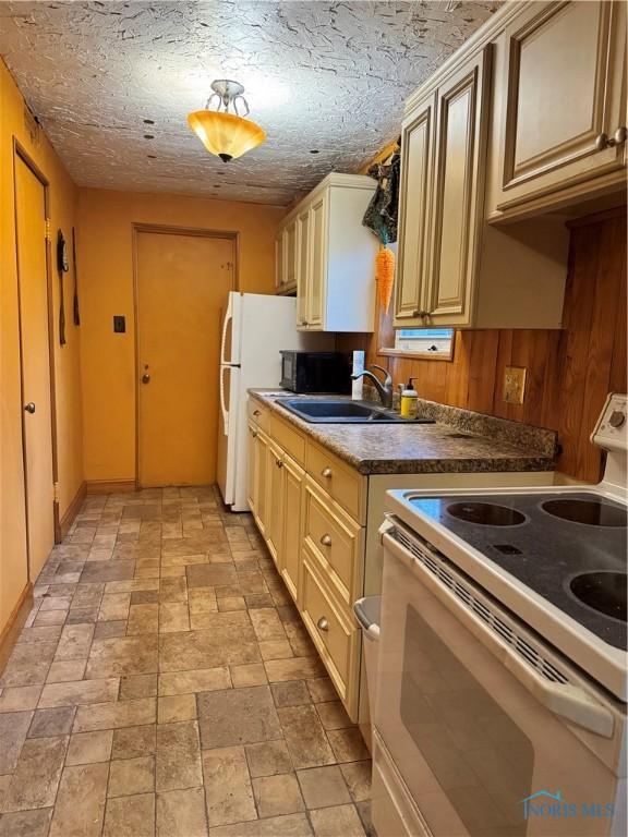 kitchen featuring white electric stove, dark countertops, stone finish flooring, black microwave, and a sink