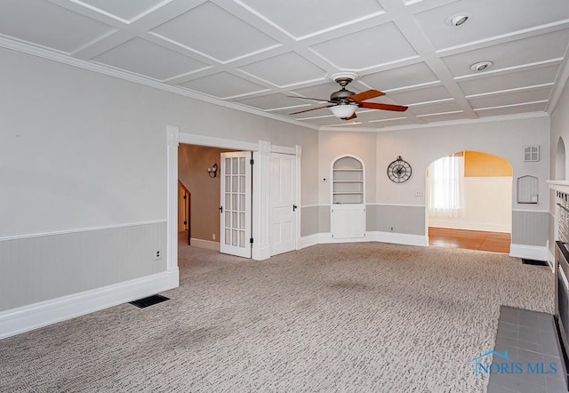 unfurnished living room featuring arched walkways, a wainscoted wall, coffered ceiling, carpet flooring, and a ceiling fan