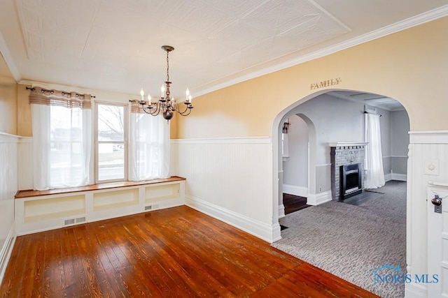 unfurnished dining area featuring dark wood-style flooring, wainscoting, a fireplace with flush hearth, and visible vents