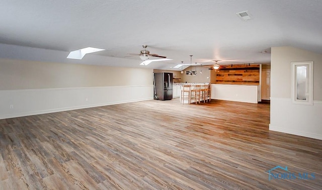 unfurnished living room with lofted ceiling with skylight, visible vents, ceiling fan, and wood finished floors