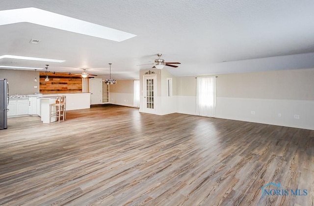 unfurnished living room with lofted ceiling with skylight, ceiling fan, visible vents, and wood finished floors