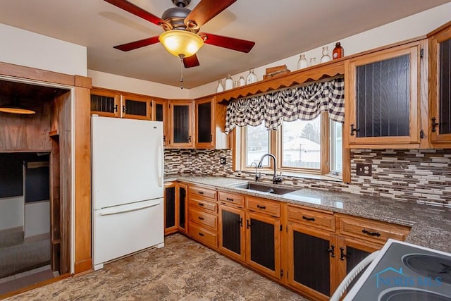 kitchen featuring stone counters, freestanding refrigerator, brown cabinetry, and a sink