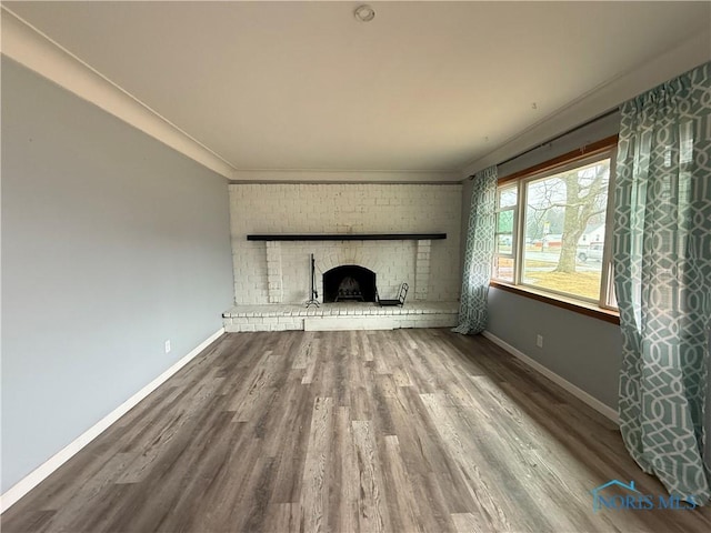 unfurnished living room with crown molding, a fireplace, baseboards, and wood finished floors