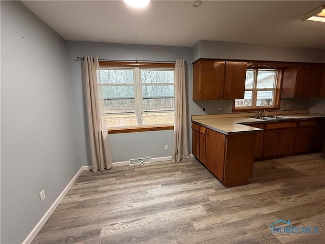 kitchen featuring brown cabinets, light wood-style flooring, light countertops, and a sink