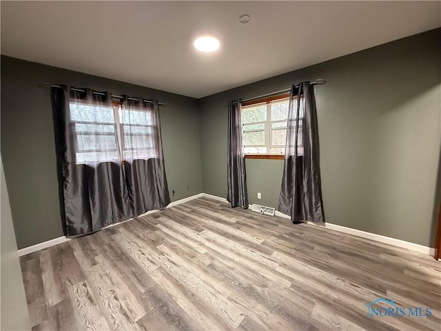 spare room with visible vents, wood finished floors, a wealth of natural light, and baseboards