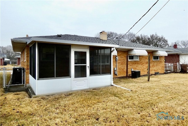 back of property with a lawn, a sunroom, a chimney, fence, and brick siding