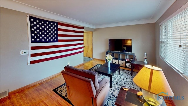 living room featuring visible vents, crown molding, baseboards, and wood finished floors