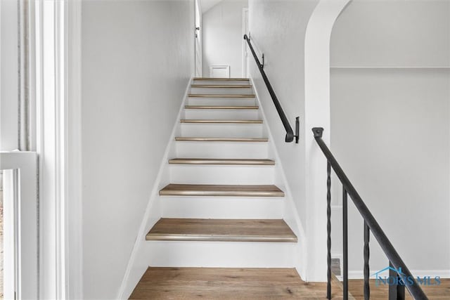 staircase featuring arched walkways and wood finished floors