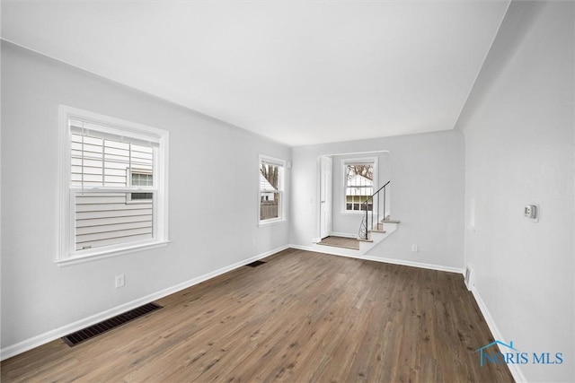 empty room featuring stairs, wood finished floors, visible vents, and baseboards