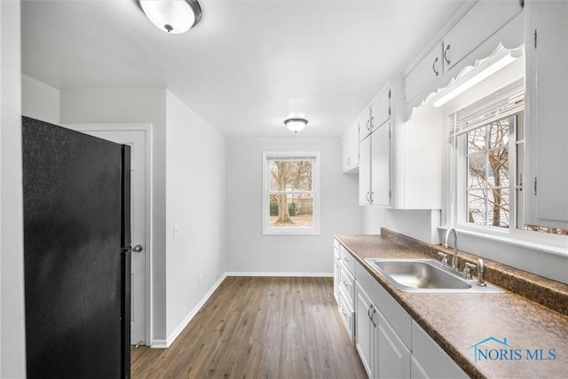 kitchen with baseboards, wood finished floors, a sink, and white cabinets