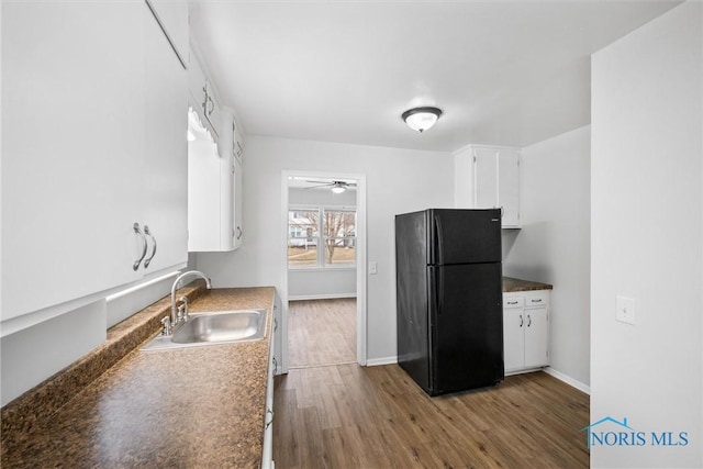 kitchen featuring dark wood-style floors, freestanding refrigerator, white cabinetry, a sink, and baseboards