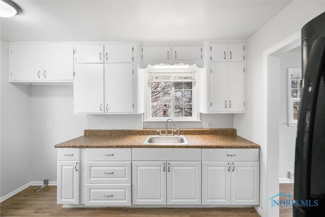 kitchen with dark countertops, white cabinetry, a sink, and wood finished floors