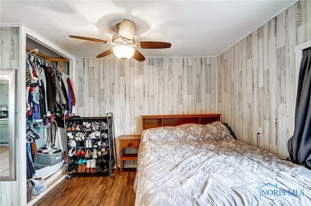 bedroom featuring a textured ceiling, ceiling fan, wooden walls, and wood finished floors