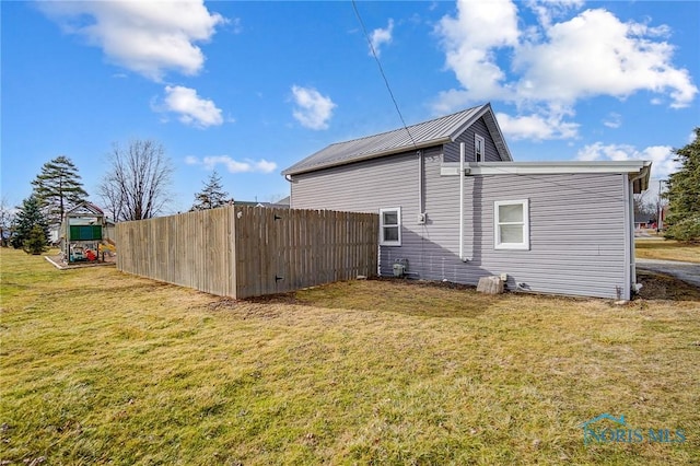 view of side of home with metal roof, a lawn, a playground, and fence