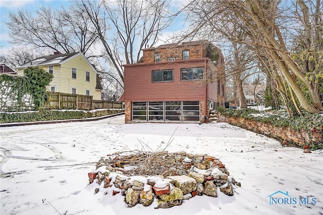 snow covered property featuring brick siding and fence