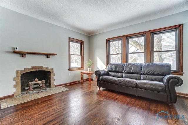 living area with dark wood-type flooring, baseboards, a textured ceiling, and a fireplace with flush hearth