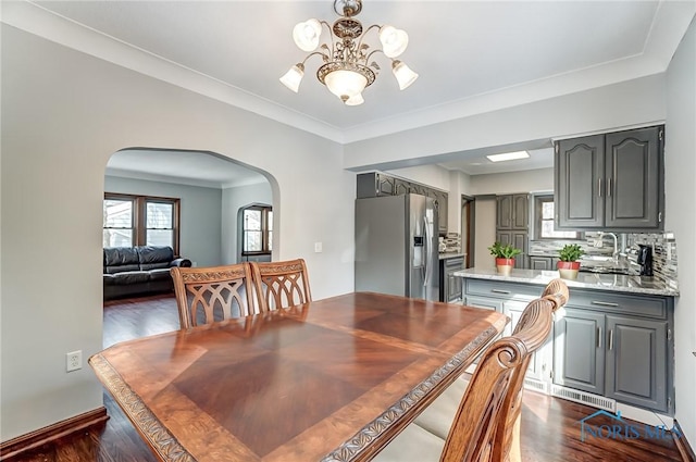 dining room featuring arched walkways, ornamental molding, dark wood-style flooring, and a chandelier