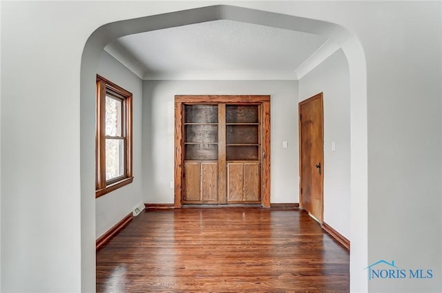 spare room with arched walkways, dark wood-style flooring, and baseboards