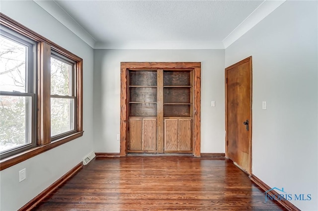 empty room featuring a textured ceiling, dark wood finished floors, visible vents, and baseboards