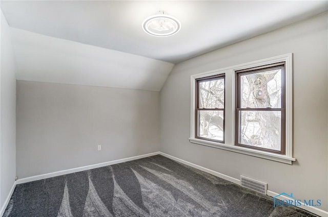 additional living space with lofted ceiling, dark carpet, visible vents, and baseboards