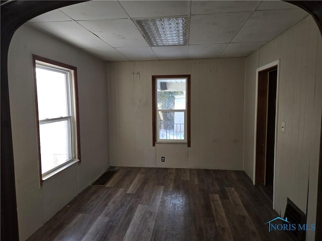 unfurnished room featuring dark wood-style floors, arched walkways, and a drop ceiling