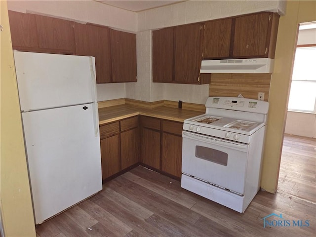 kitchen with under cabinet range hood, white appliances, light countertops, brown cabinets, and dark wood finished floors