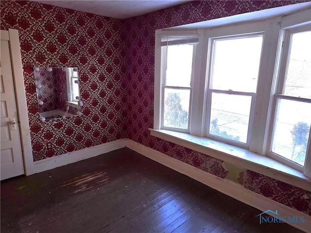 unfurnished room with dark wood-type flooring, baseboards, and wallpapered walls