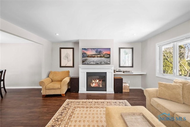 living area with dark wood-style floors, recessed lighting, a glass covered fireplace, and baseboards