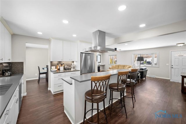 kitchen with dark countertops, appliances with stainless steel finishes, white cabinets, island range hood, and a kitchen breakfast bar