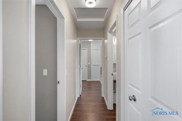 hall featuring dark wood-type flooring, attic access, and baseboards