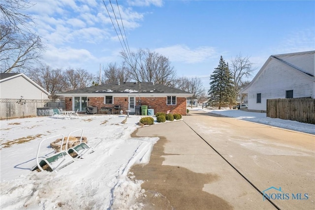 snow covered rear of property featuring brick siding and fence