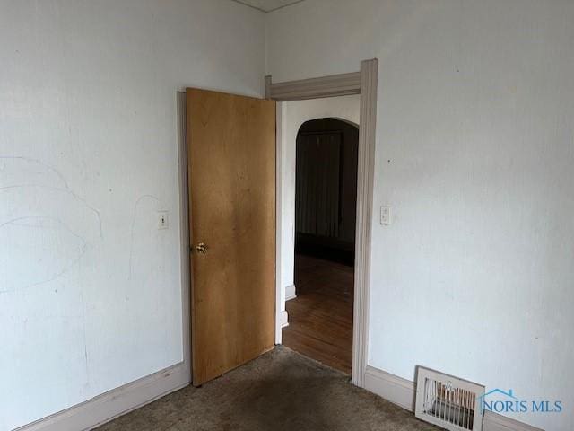 empty room featuring visible vents, arched walkways, and dark colored carpet