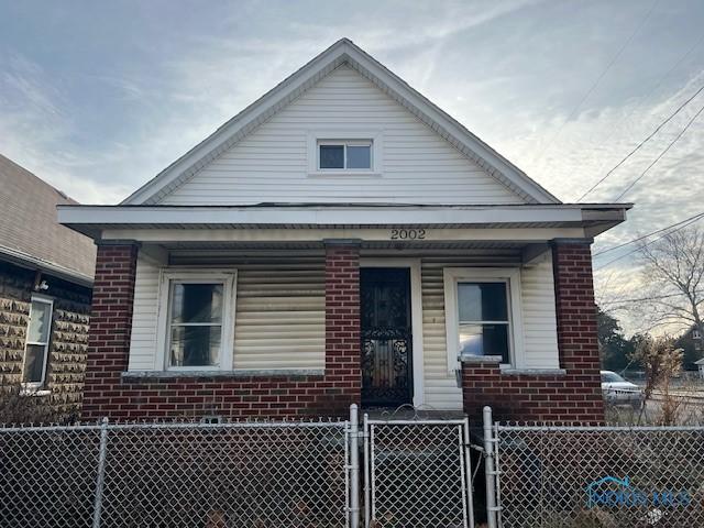 bungalow-style house with a fenced front yard, a porch, and brick siding