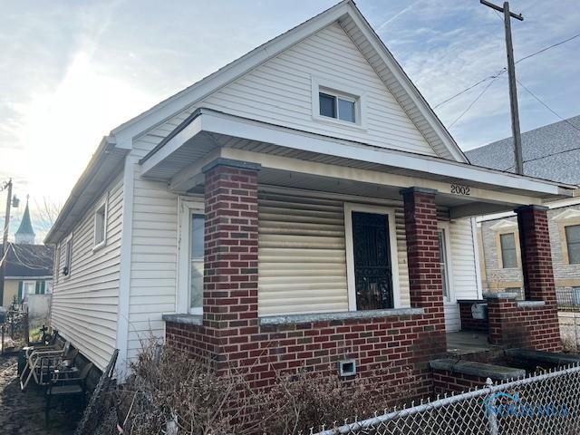 view of home's exterior featuring covered porch, brick siding, and fence